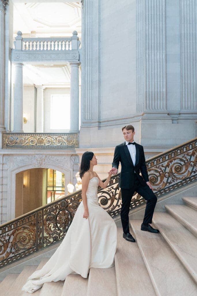 Couple walking up the grand staircase at San Francisco City Hall, groom leading bride