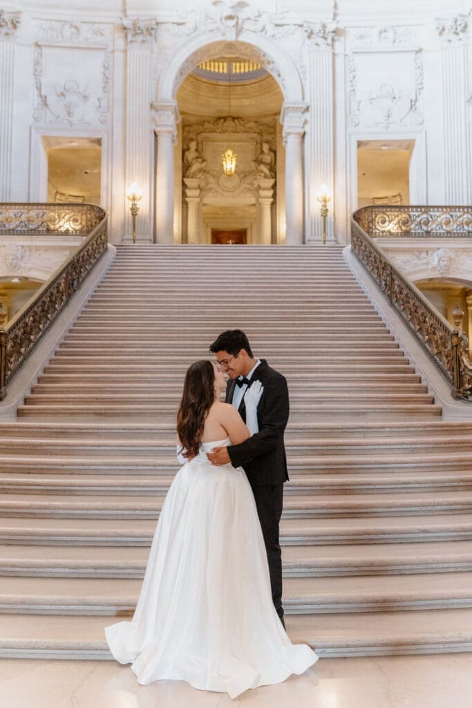 Couple standing at the bottom of the San Francisco City Hall grand staircase in wedding attire