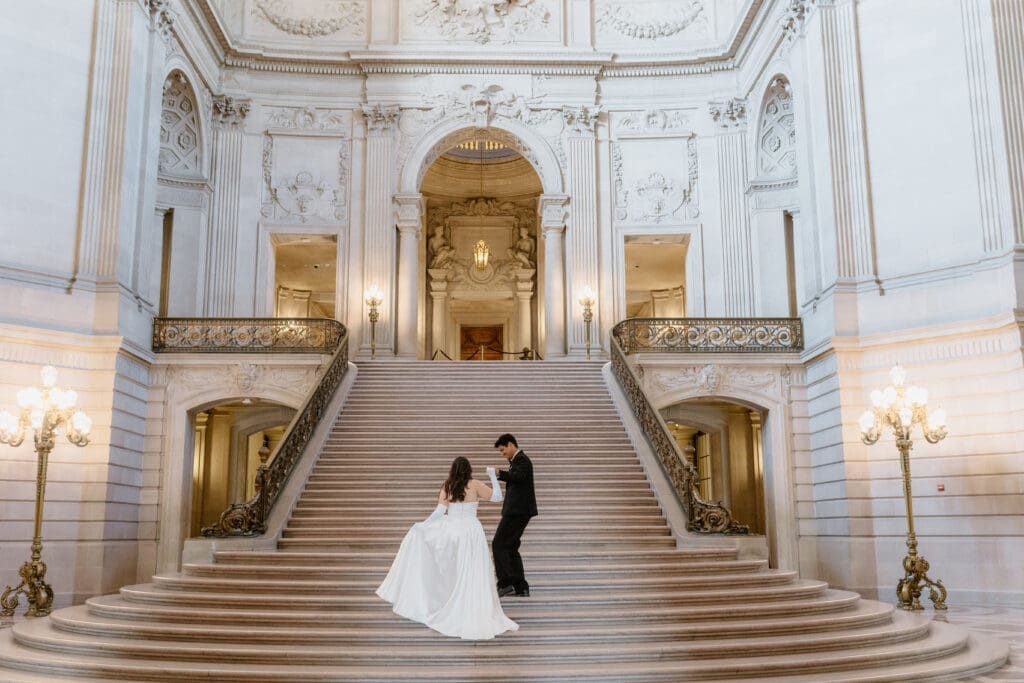 San Francisco City Hall couple walking up the grand staircase, bride in silk gown with train and groom in black tux